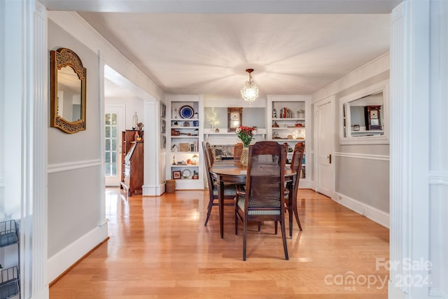 dining area with a chandelier, light wood-type flooring, and built in shelves