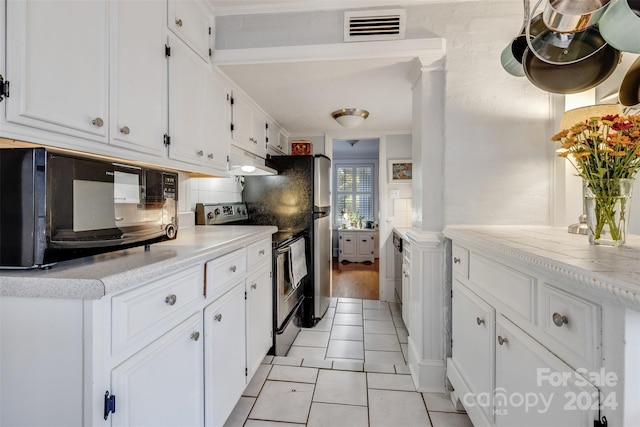 kitchen featuring stainless steel electric stove, white cabinets, light tile patterned floors, and backsplash