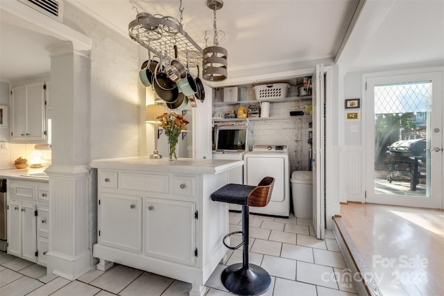 kitchen featuring white cabinetry, washing machine and dryer, decorative light fixtures, and a kitchen breakfast bar