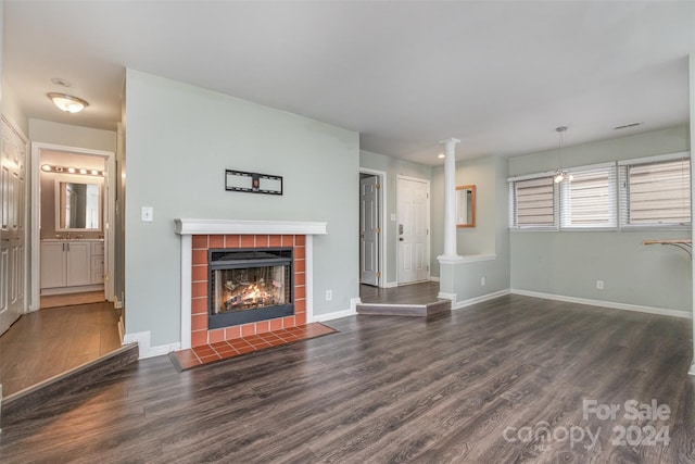 unfurnished living room featuring a tile fireplace, dark wood-type flooring, and ornate columns