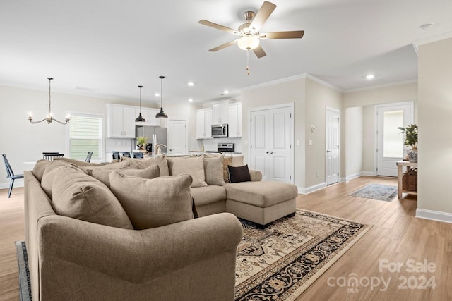 living room with ceiling fan with notable chandelier, light hardwood / wood-style flooring, and ornamental molding