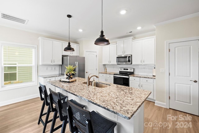 kitchen with stainless steel appliances, a kitchen bar, sink, white cabinets, and light hardwood / wood-style flooring