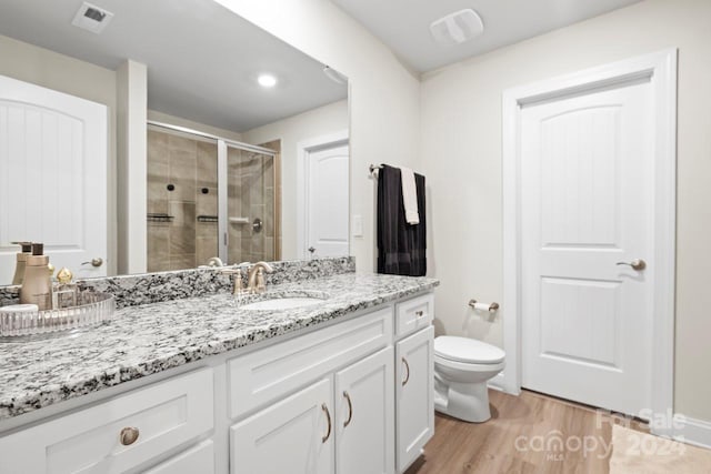 bathroom featuring wood-type flooring, toilet, vanity, and a shower with shower door