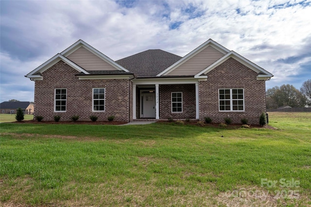 craftsman inspired home featuring roof with shingles, a front yard, and brick siding