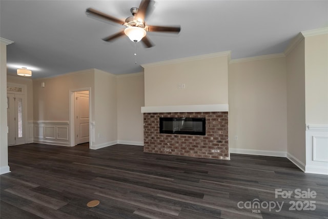 unfurnished living room with a decorative wall, dark wood-style flooring, a fireplace, a ceiling fan, and ornamental molding