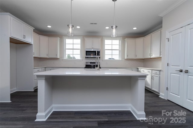 kitchen featuring a kitchen island with sink, a sink, white cabinetry, decorative backsplash, and stainless steel microwave