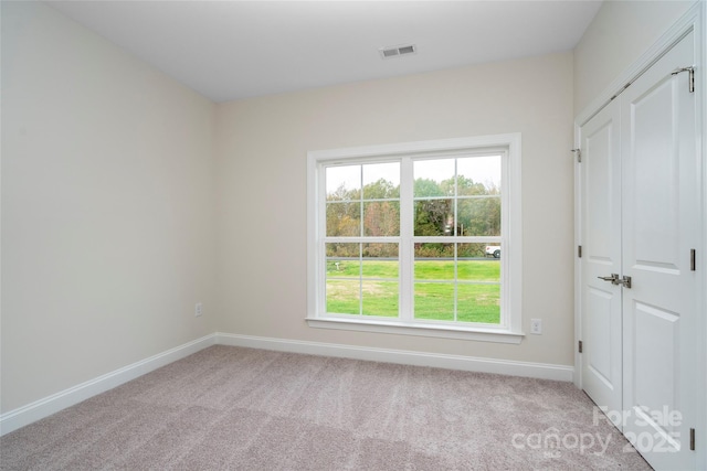 unfurnished room with carpet, visible vents, and baseboards