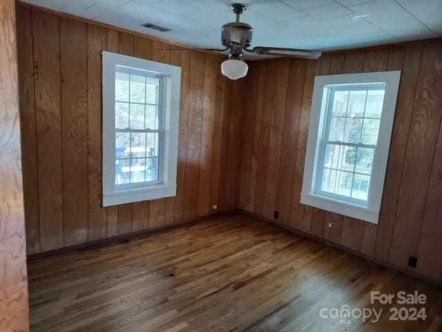 unfurnished dining area featuring ceiling fan, hardwood / wood-style flooring, a healthy amount of sunlight, and wood walls