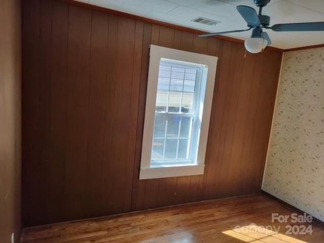 empty room with ornamental molding, ceiling fan, light hardwood / wood-style floors, and wood walls