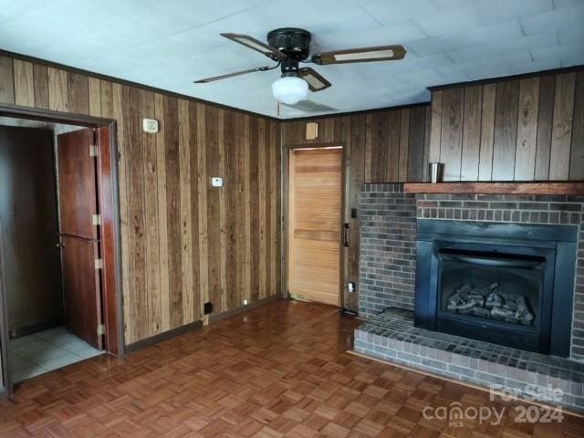 unfurnished living room with dark parquet floors, wooden walls, a fireplace, and ceiling fan