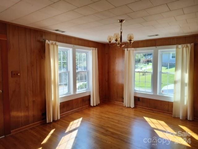 unfurnished room with hardwood / wood-style flooring, a chandelier, and wooden walls