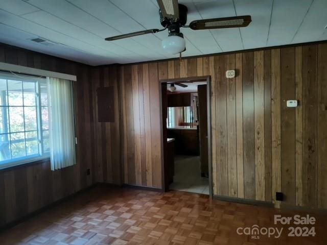 spare room with ceiling fan, wood walls, and parquet floors