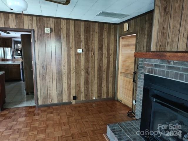 unfurnished living room with a brick fireplace, wooden walls, and dark parquet flooring