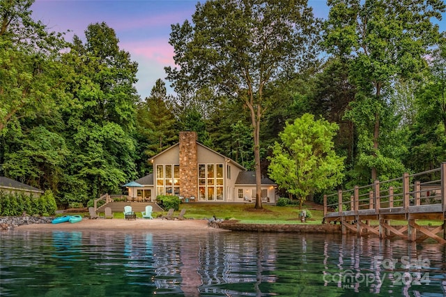 back house at dusk with a deck with water view and a lawn