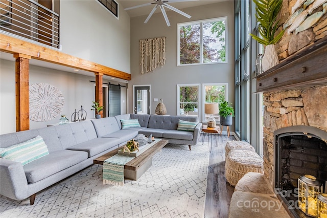 living room with a fireplace, a barn door, hardwood / wood-style floors, ceiling fan, and a high ceiling