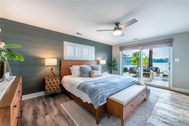 bedroom featuring wood walls, dark wood-type flooring, access to outside, and ceiling fan