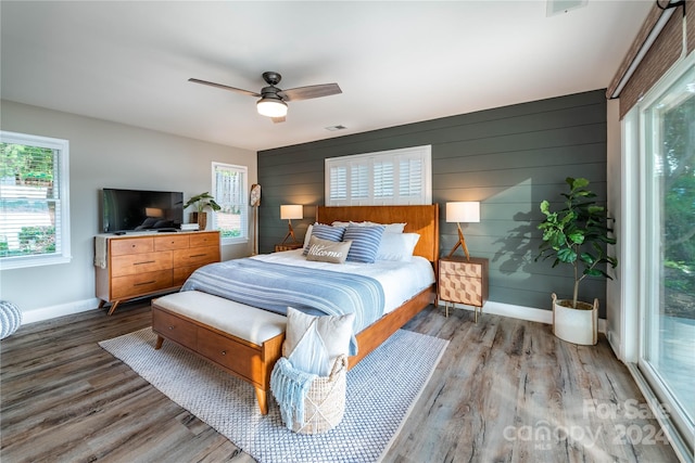 bedroom featuring ceiling fan, hardwood / wood-style flooring, wood walls, and access to exterior