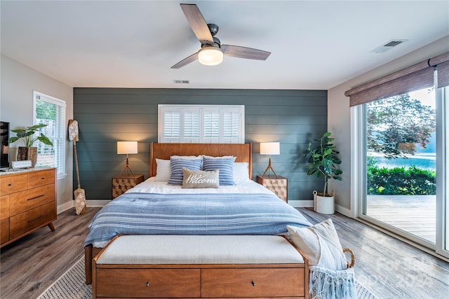 bedroom with access to outside, hardwood / wood-style floors, wood walls, and ceiling fan