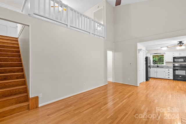 unfurnished living room with ceiling fan, light wood-type flooring, sink, and a towering ceiling