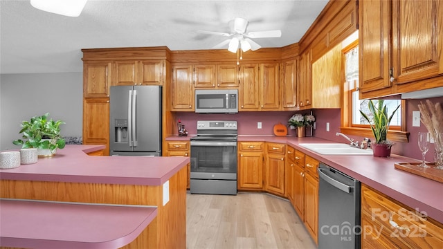 kitchen with appliances with stainless steel finishes, light wood-type flooring, ceiling fan, and sink