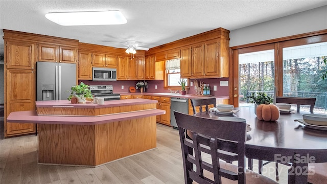 kitchen featuring ceiling fan, a center island, a textured ceiling, appliances with stainless steel finishes, and light wood-type flooring