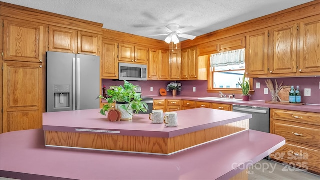 kitchen featuring appliances with stainless steel finishes, a textured ceiling, ceiling fan, sink, and a center island