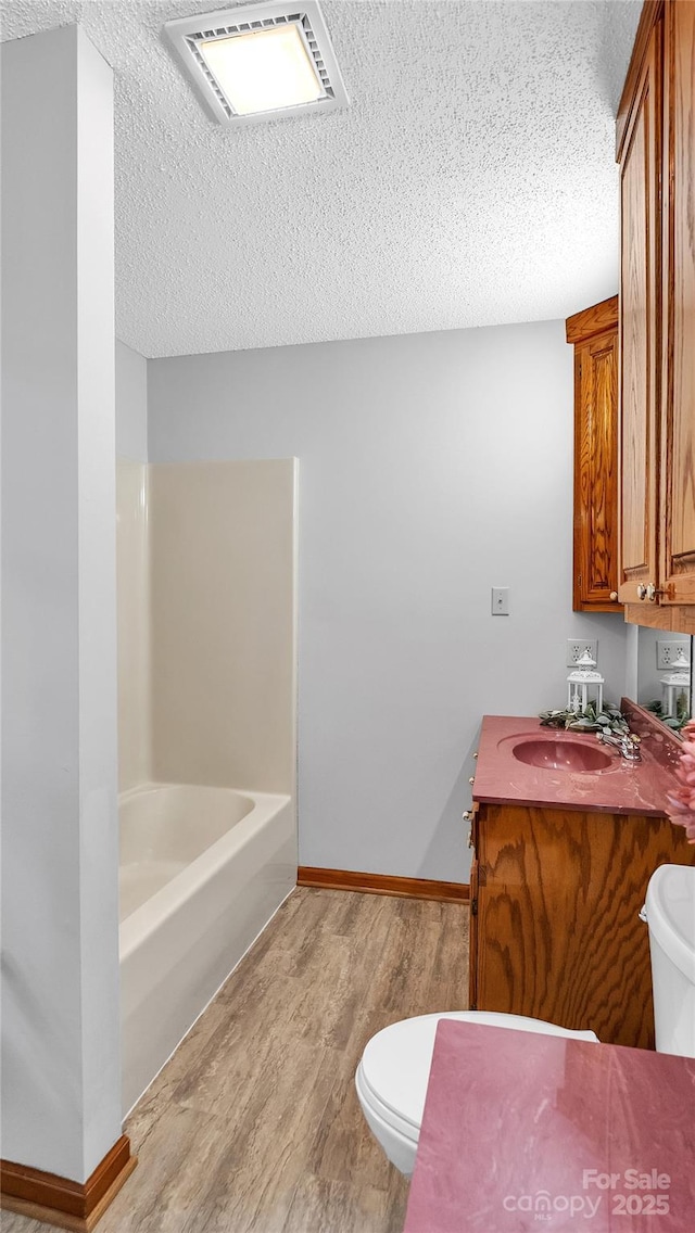 bathroom with vanity, a washtub, toilet, a textured ceiling, and wood-type flooring