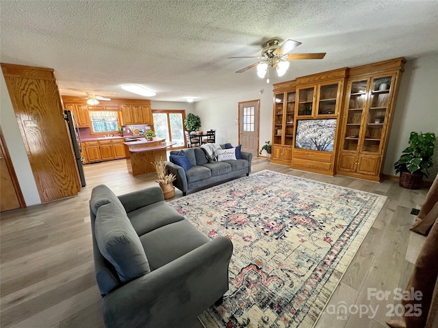 living room with a textured ceiling, light hardwood / wood-style floors, and ceiling fan