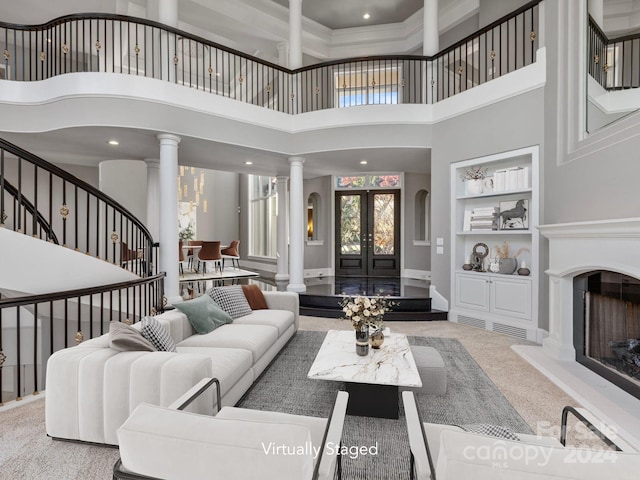 carpeted living room with french doors, built in features, a towering ceiling, and decorative columns