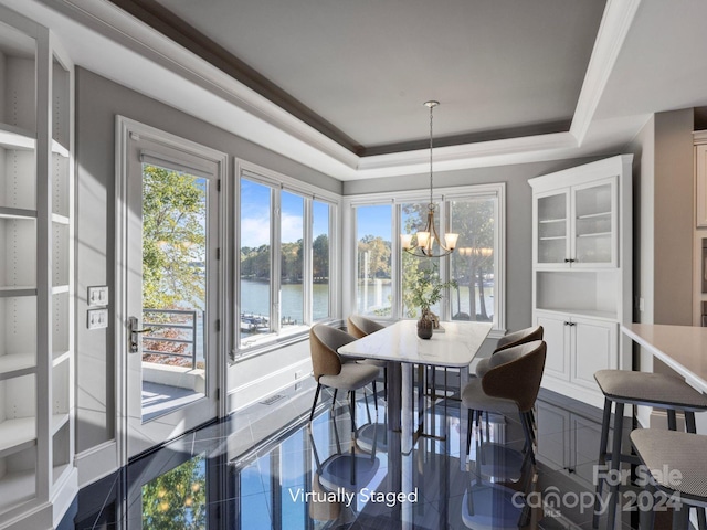 tiled dining room featuring an inviting chandelier, a tray ceiling, and a water view