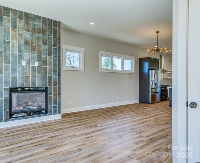 unfurnished living room with a tile fireplace, an inviting chandelier, and light hardwood / wood-style flooring