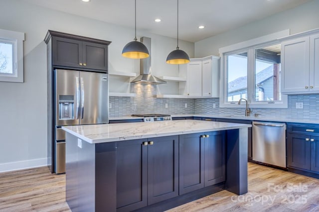 kitchen featuring white cabinets, appliances with stainless steel finishes, a kitchen island, hanging light fixtures, and ventilation hood