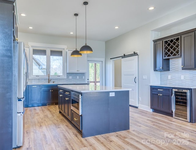 kitchen with a barn door, appliances with stainless steel finishes, wine cooler, a kitchen island, and pendant lighting