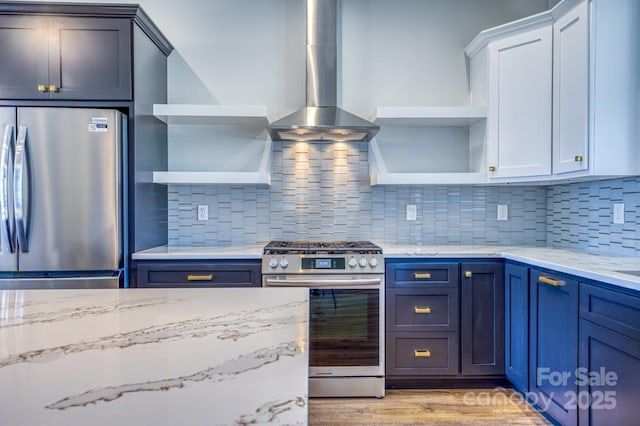 kitchen with backsplash, wall chimney range hood, stainless steel appliances, white cabinets, and blue cabinets