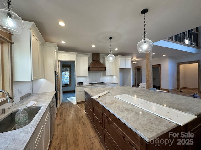 kitchen featuring a spacious island, appliances with stainless steel finishes, light wood-style floors, premium range hood, and a sink