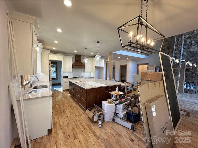 kitchen featuring light wood-style flooring, premium range hood, a sink, white cabinets, and a center island