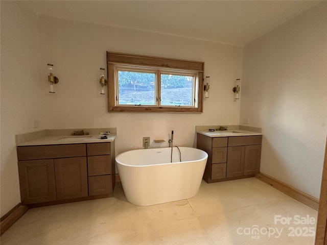 bathroom featuring a freestanding bath, a sink, two vanities, and baseboards