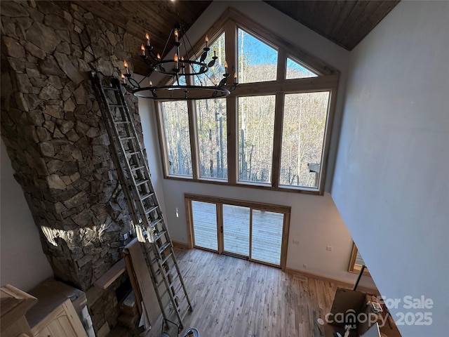 unfurnished living room featuring high vaulted ceiling, baseboards, an inviting chandelier, and wood finished floors