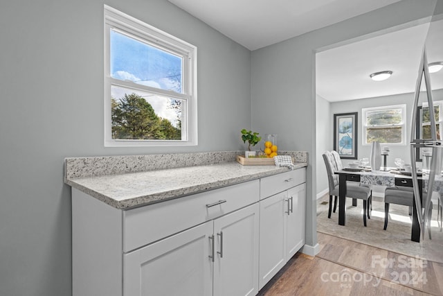 kitchen with white cabinetry, light stone counters, and light hardwood / wood-style floors