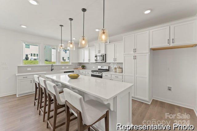 kitchen with appliances with stainless steel finishes, sink, light wood-type flooring, a kitchen island, and white cabinets