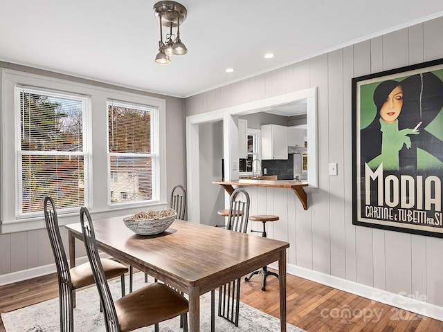 dining space with crown molding, light hardwood / wood-style flooring, wood walls, and sink