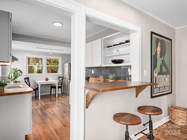 kitchen featuring hardwood / wood-style flooring, decorative backsplash, butcher block counters, a breakfast bar area, and stainless steel refrigerator