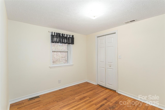 unfurnished bedroom featuring wood-type flooring, a closet, and a textured ceiling