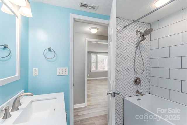 bathroom featuring vanity, a textured ceiling, tiled shower / bath, and hardwood / wood-style flooring