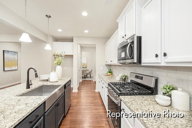 kitchen with sink, appliances with stainless steel finishes, decorative light fixtures, and white cabinetry