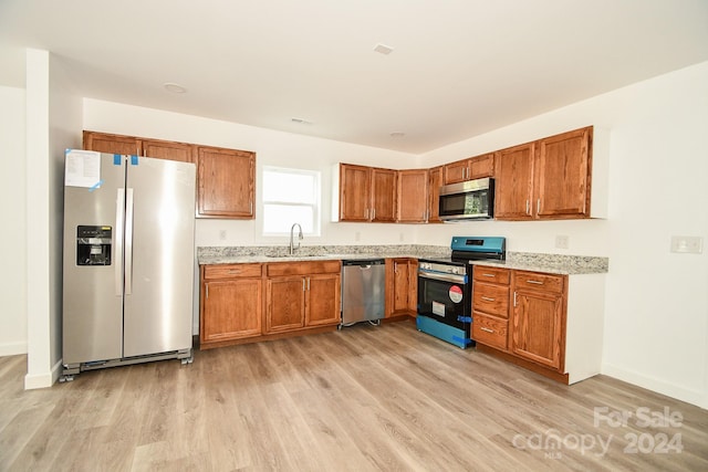 kitchen with appliances with stainless steel finishes, sink, and light wood-type flooring