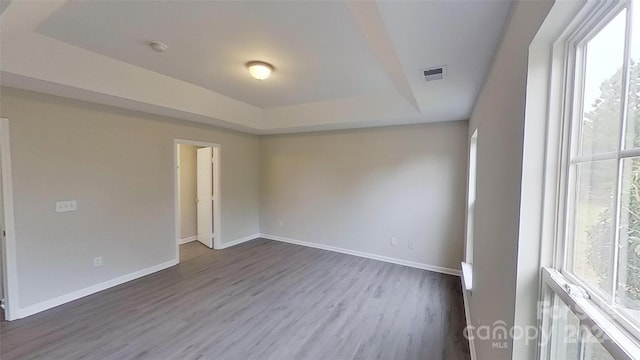 unfurnished room with plenty of natural light, a tray ceiling, and dark hardwood / wood-style flooring