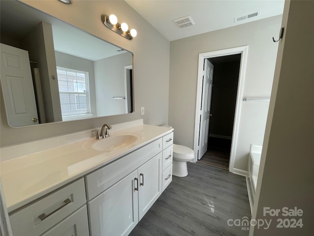 bathroom featuring toilet, a bath, vanity, and hardwood / wood-style floors