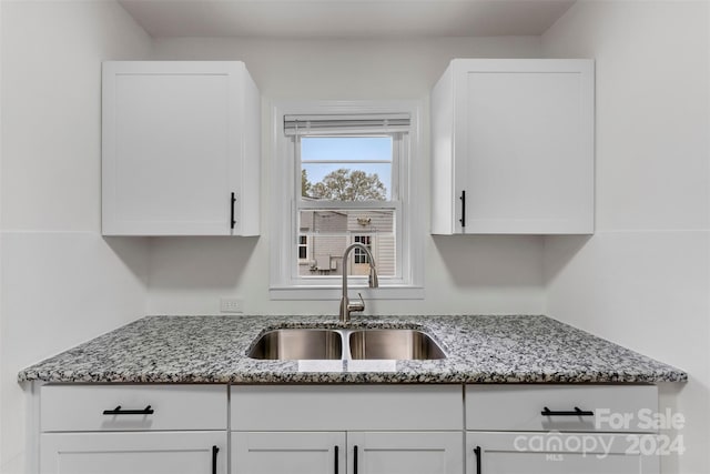 kitchen with light stone countertops, white cabinetry, and sink