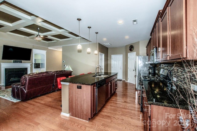 kitchen featuring a center island with sink, dark stone counters, light hardwood / wood-style floors, sink, and coffered ceiling